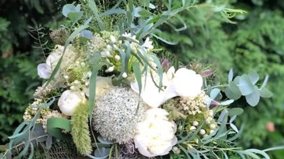 Ein Blumenstrauß wird gehalten, umgeben von grünen Pflanzen.