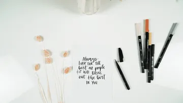 Card with inspirational text next to pens and dried flowers