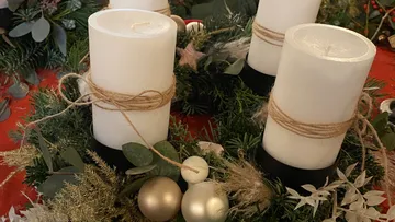 White candles are on a festively decorated wreath.
