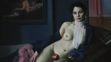 A naked woman with an apple lying on a bed.