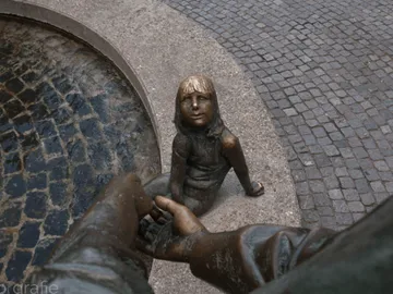 Bronzestatue eines Kindes, das eine Hand hält, am Brunnen.