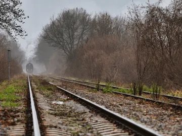 Steam locomotive travels through foggy, deserted surroundings along tracks.
