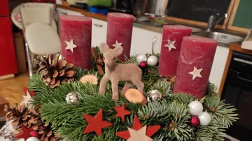 Adventskranz mit roten Kerzen, Tannenzweigen und dekorierten Figuren.