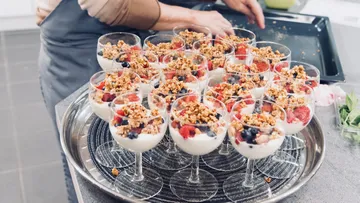 Dessertgläser mit Joghurt, Früchten und Granola auf Tablett.