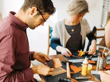 Two people are working on a craft project at the table.