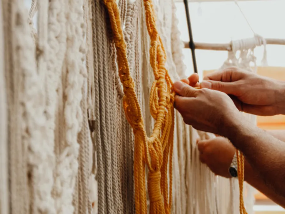 Hands tie yellow yarn between white threads.