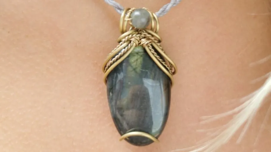 A pendant hangs from a necklace, shiny and ornately decorated.