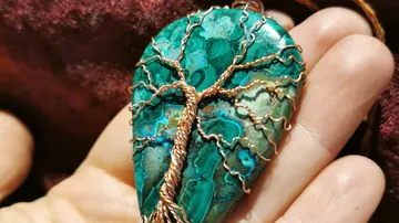 Hand details hold a hanging ornament with a tree design.