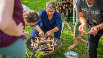 Frau zündet Holz in einer Feuerschale im Freien an.