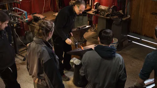 Schmied arbeitet mit einem glühenden Metallstück am Amboss.