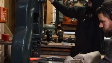 Eine Presse bearbeitet Metall, während Arbeiter assistieren.
