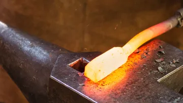 A glowing piece of metal is forged on an anvil.