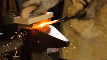 Ein Schmied bearbeitet glühendes Metall auf einem Amboss.