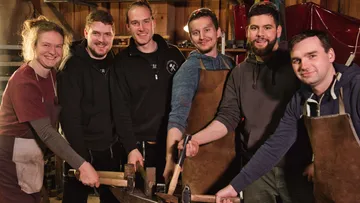 Six craftsmen hold tools together in a workshop.