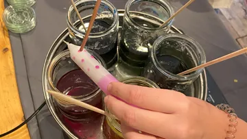 Eine Hand hält eine Kerze über bunte Farbgläser.