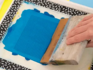 Eine Hand drückt einen Farbroller auf eine blaue Fläche.