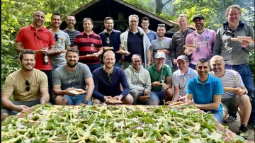 Gruppe von Männern posiert mit Essen im Wald.