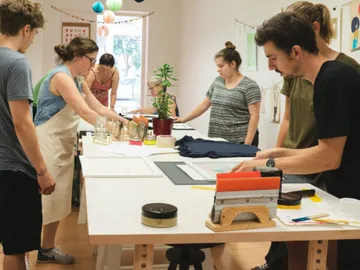 Gruppenschulung, Menschen arbeiten an Tischen in kreativem Raum.