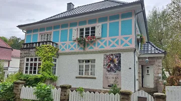 Colourfully painted house with flowers and fence in nature.