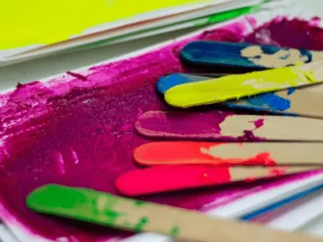 Farben auf Holzstäbchen liegen in lila Farbe.