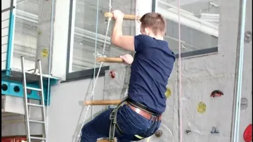 Junger Mann klettert an einer Leiter in einer Sporthalle.
