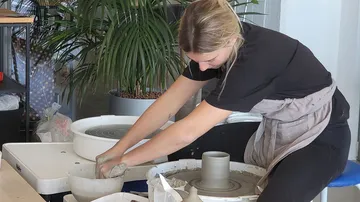 A woman sculpts clay on a pottery machine in a studio.
