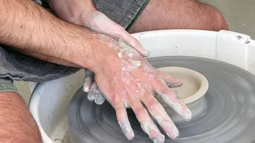 Hands form a clay cup on a potter's wheel.