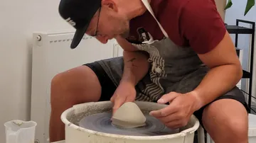 Man forms clay on a potter's wheel in a studio.
