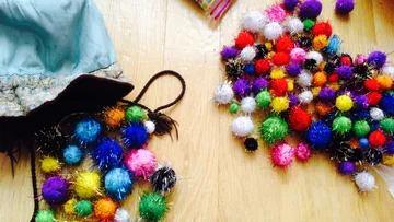 Bunte Pompons liegen verstreut auf dem Boden, neben einer Bluse.