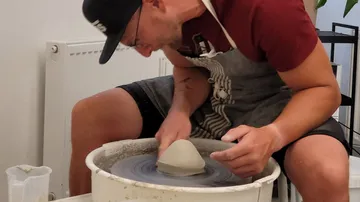 Ein Töpfer formt Ton auf einer Drehscheibe in einem Atelier.