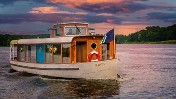 Ein Boot fährt über einen ruhigen Fluss bei Sonnenuntergang.