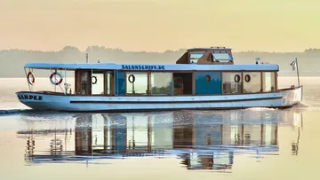 Ein Schiff fährt über ruhiges Wasser im Morgenlicht.