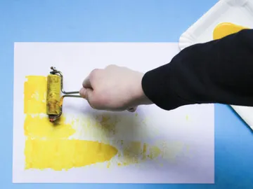 Eine Hand rollt gelbe Farbe auf weißes Papier.