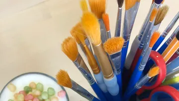 Pinsel stehen in einem Behälter neben bunten Süßigkeiten.
