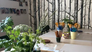 Tisch mit Pflanzen und Buntstiften vor Baumtapete.