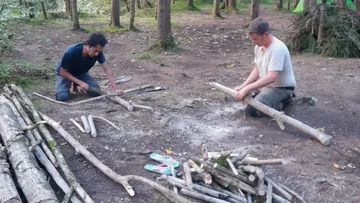 Zwei Männer bearbeiten Holzstücke im Wald.