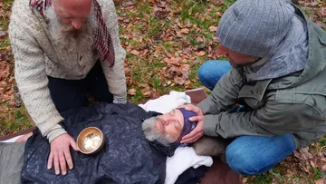 Drei Personen helfen einem Verletzten im Wald.