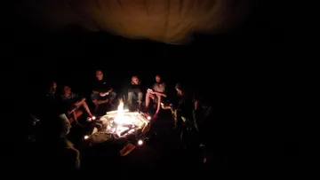 Lagerfeuer leuchtet, Menschen sitzen im Dunkeln und erzählen Geschichten.