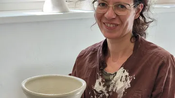 Woman holding a clay cup in a room full of light.