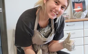 Junge Frau formt Ton und lächelt in einem Atelier.