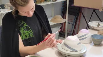 Eine Frau bemalt eine Tasse in einem Atelier.