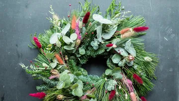 Kranz aus verschiedenen grünen Pflanzen und bunten Blüten.