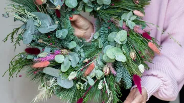 Ein Mensch hält einen bunten, floralen Kranz in den Händen.