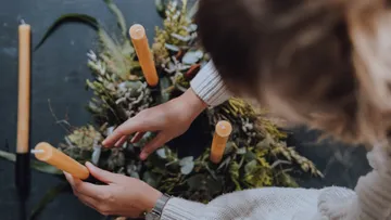 Hands form a wreath with candles in a green environment.