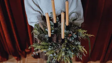 A person is holding a decorative wreath with candles.