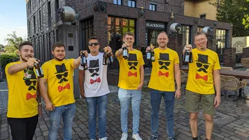 Sechs Männer, lächelnd, halten Bierflaschen vor einem Restaurant.