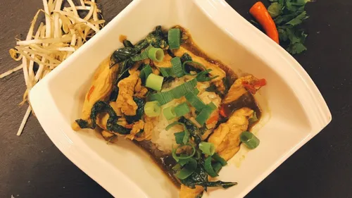 Gericht mit Hähnchen, Reis und frischem Gemüse in Schale.