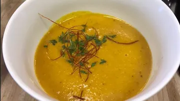 Soup in white bowl decorated with herbs and threads.