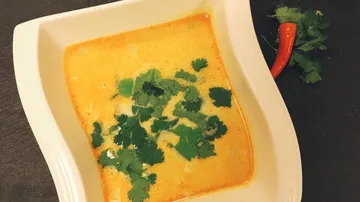 Creamy soup with coriander and chilli on a white plate.