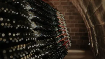 Wine bottles are piled up in a cellar with brick walls.